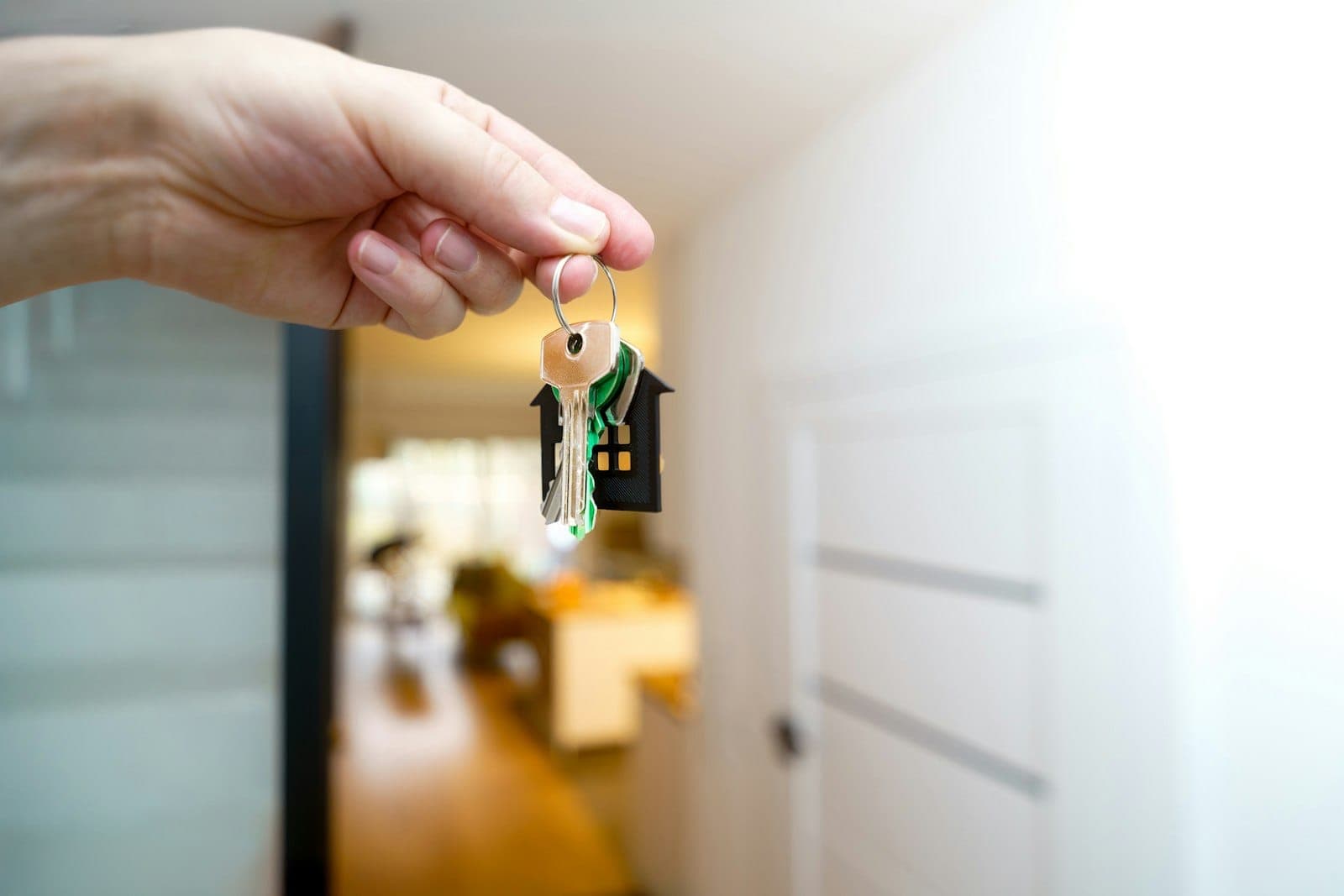 A hand holding a set of keys with a house keyring in a bright hallway