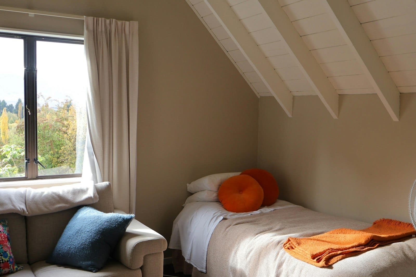 A single bed under a sloping roof, with a window onto greenery